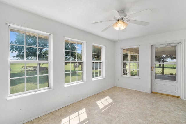 unfurnished sunroom featuring ceiling fan and a wealth of natural light