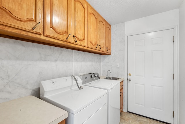 clothes washing area with cabinets, a textured ceiling, sink, and separate washer and dryer