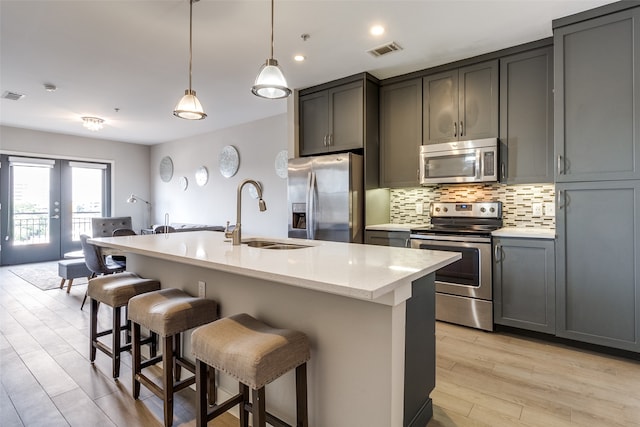 kitchen featuring appliances with stainless steel finishes, sink, light wood-type flooring, pendant lighting, and a center island with sink