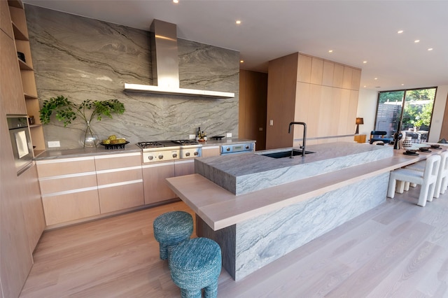 kitchen featuring sink, exhaust hood, an island with sink, and stainless steel gas cooktop