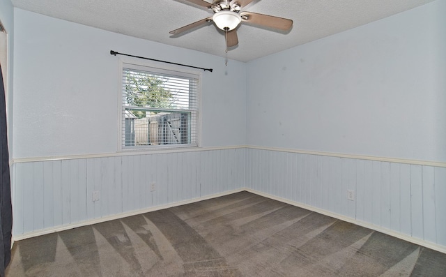 spare room with a textured ceiling, wooden walls, carpet flooring, and ceiling fan