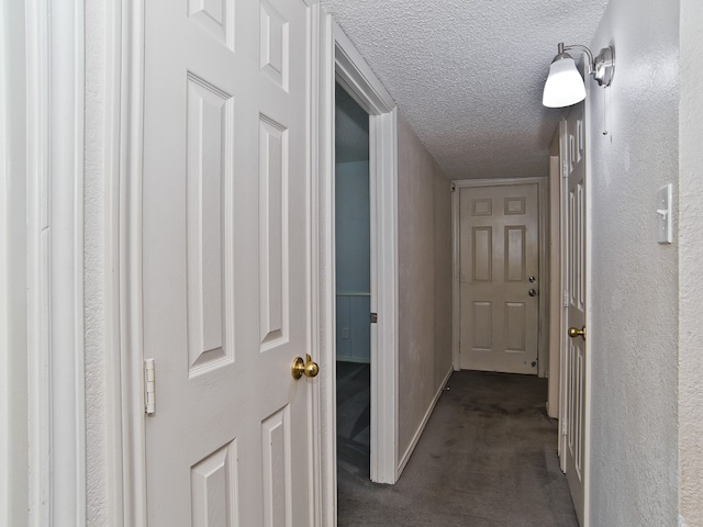 corridor featuring a textured ceiling and dark colored carpet