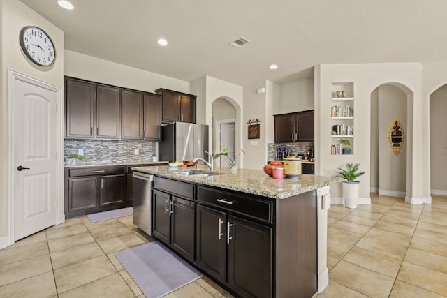 kitchen with tasteful backsplash, an island with sink, sink, dark brown cabinetry, and stainless steel appliances