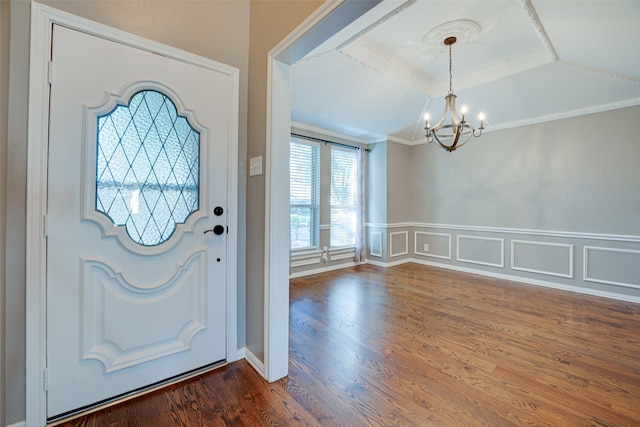 entrance foyer featuring a raised ceiling, ornamental molding, dark wood-type flooring, and a chandelier