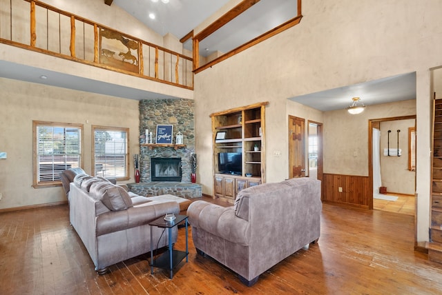 living room featuring hardwood / wood-style flooring, beamed ceiling, wooden walls, a fireplace, and high vaulted ceiling