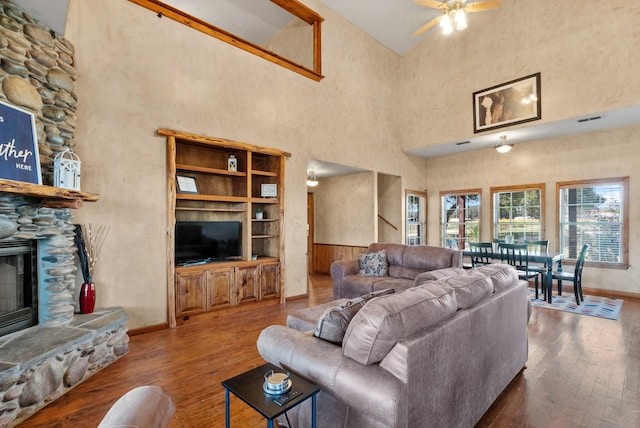 living room with ceiling fan, a fireplace, a towering ceiling, and dark hardwood / wood-style floors