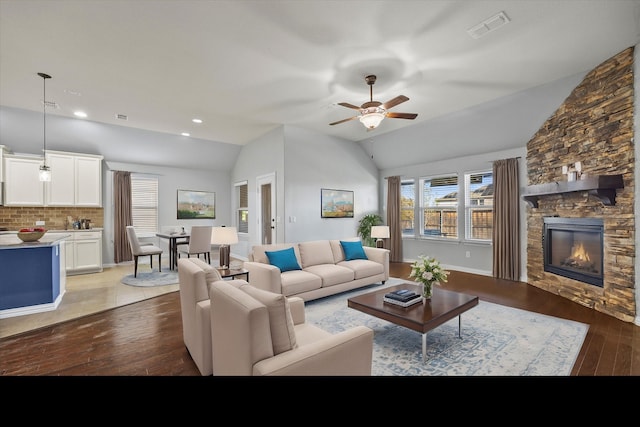 living room featuring hardwood / wood-style flooring, vaulted ceiling, a stone fireplace, and ceiling fan