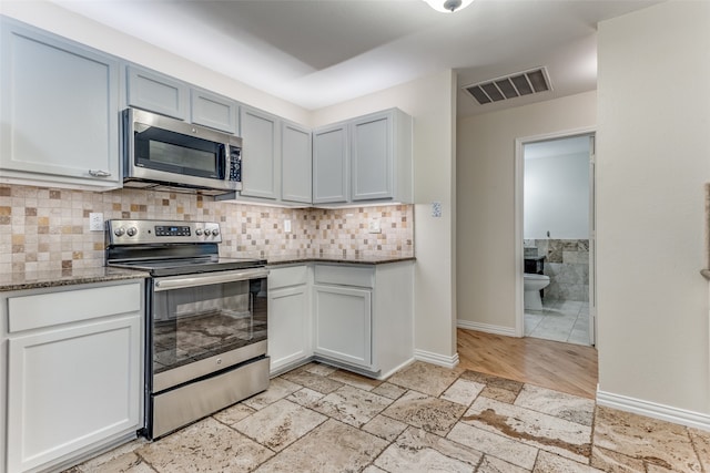 kitchen with appliances with stainless steel finishes, decorative backsplash, dark stone counters, and light wood-type flooring