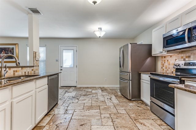 kitchen featuring white cabinetry, stainless steel appliances, backsplash, and dark stone countertops