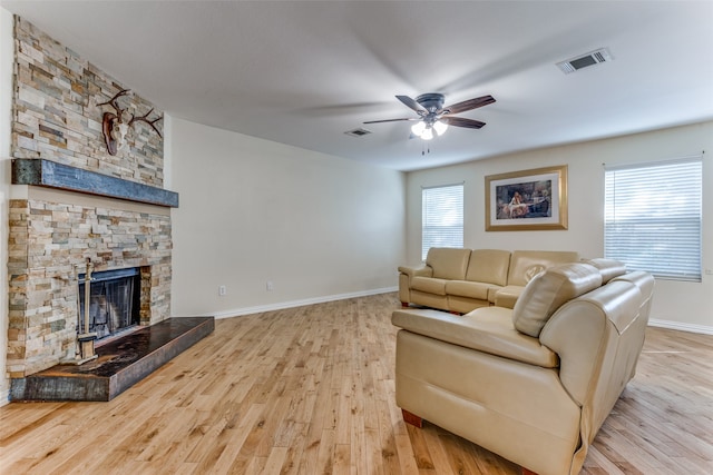 living room with ceiling fan, a stone fireplace, and light hardwood / wood-style flooring