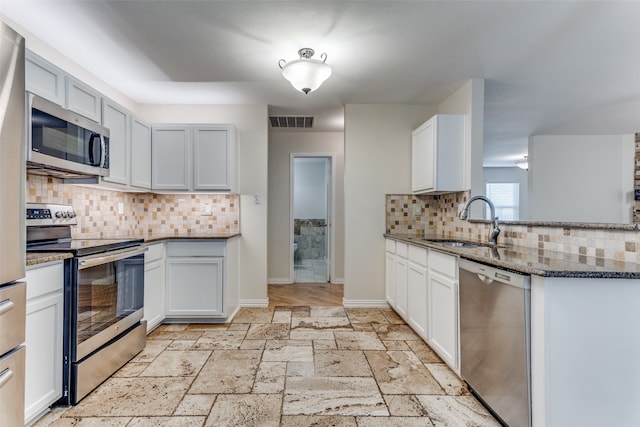 kitchen with tasteful backsplash, appliances with stainless steel finishes, sink, stone countertops, and white cabinets