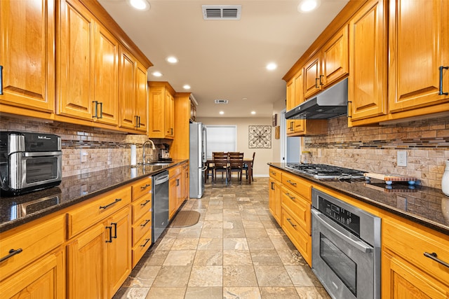 kitchen with sink, stainless steel appliances, backsplash, and dark stone counters