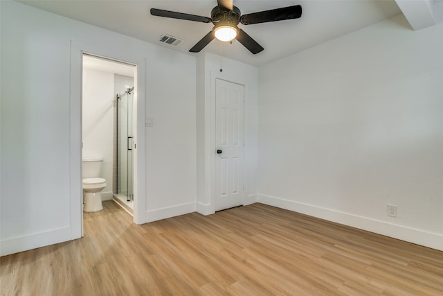 unfurnished bedroom featuring a closet, light hardwood / wood-style flooring, ensuite bath, a barn door, and ceiling fan