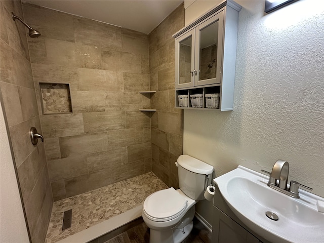 bathroom with a tile shower, toilet, and vanity