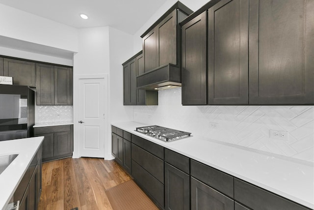 kitchen featuring black refrigerator, backsplash, dark brown cabinetry, stainless steel gas cooktop, and light hardwood / wood-style floors