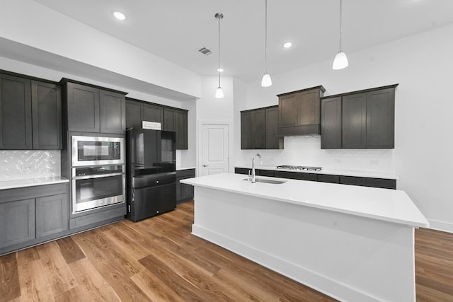 kitchen with sink, hanging light fixtures, an island with sink, wood-type flooring, and appliances with stainless steel finishes