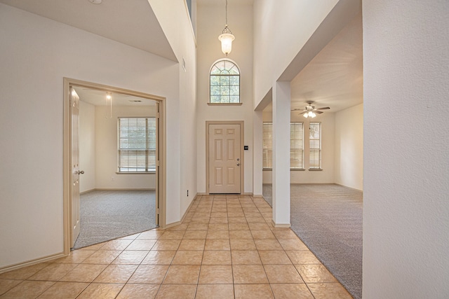 foyer entrance featuring a towering ceiling, ceiling fan, light colored carpet, and a wealth of natural light