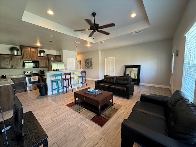 living room with light hardwood / wood-style flooring, a tray ceiling, and ceiling fan