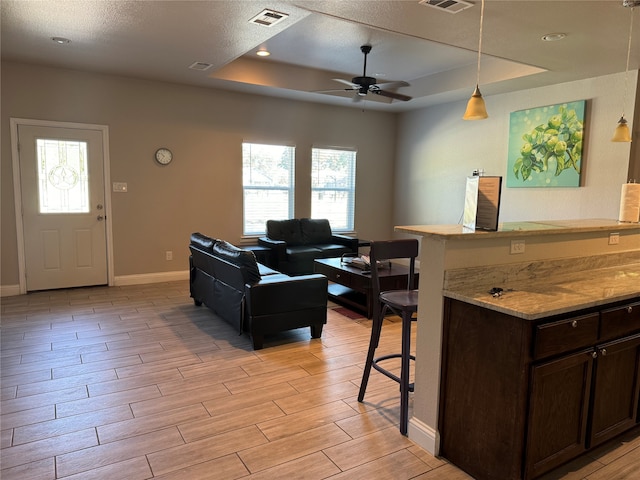 living room with light hardwood / wood-style floors, a tray ceiling, and ceiling fan