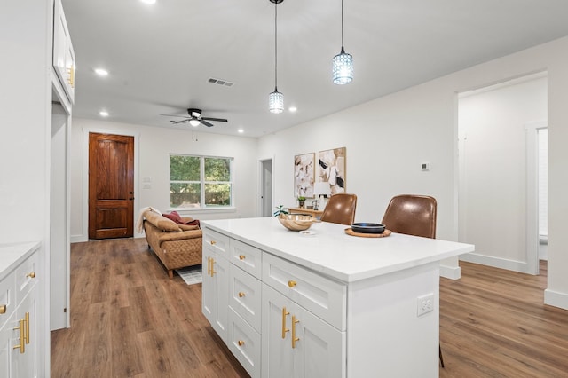 kitchen featuring a breakfast bar, white cabinets, hanging light fixtures, light hardwood / wood-style flooring, and ceiling fan