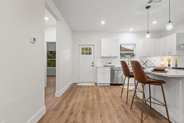 kitchen featuring light wood-type flooring, white cabinetry, hanging light fixtures, and stainless steel dishwasher