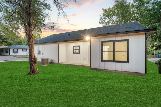 back house at dusk with cooling unit and a lawn