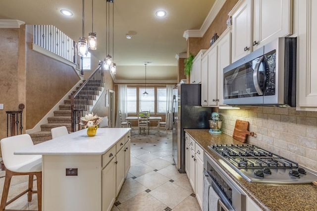 kitchen with a kitchen island, a breakfast bar area, hanging light fixtures, ornamental molding, and appliances with stainless steel finishes