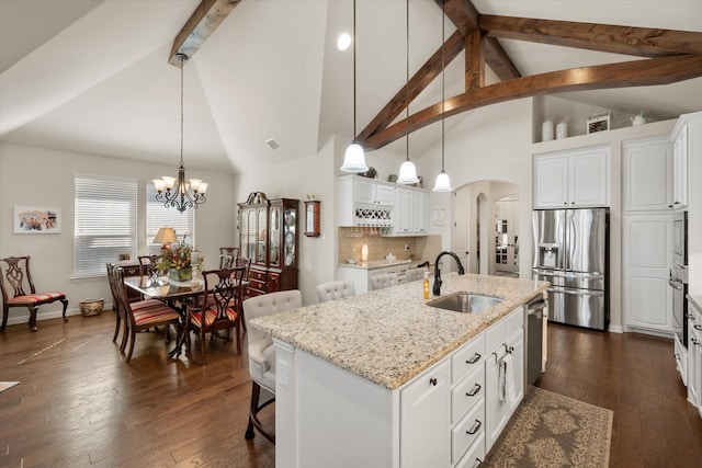 kitchen with sink, hanging light fixtures, white cabinetry, stainless steel appliances, and a center island with sink