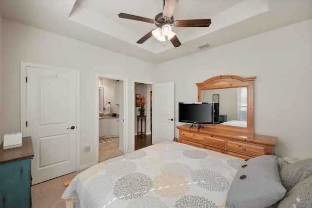 bedroom with ensuite bath, a tray ceiling, and ceiling fan