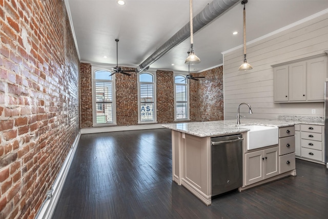 kitchen featuring light stone countertops, sink, hanging light fixtures, brick wall, and stainless steel dishwasher