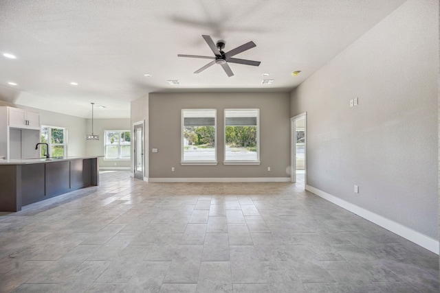 unfurnished living room with sink, a textured ceiling, and ceiling fan with notable chandelier