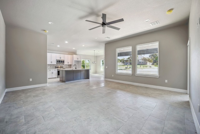 unfurnished living room featuring sink, ceiling fan, a textured ceiling, and plenty of natural light