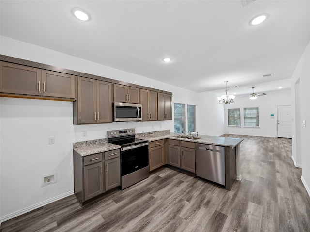 kitchen featuring kitchen peninsula, stainless steel appliances, wood-type flooring, pendant lighting, and ceiling fan with notable chandelier