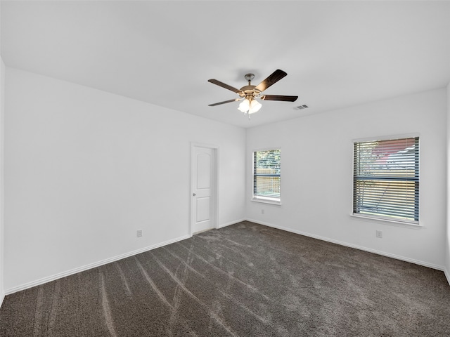 spare room with ceiling fan, a healthy amount of sunlight, and dark carpet