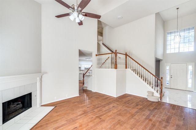 unfurnished living room with a towering ceiling, ceiling fan with notable chandelier, a tile fireplace, and light wood-type flooring