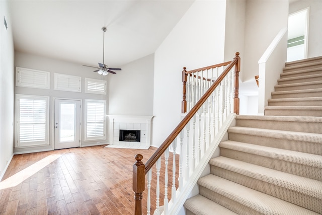 stairway with a tiled fireplace, wood-type flooring, a high ceiling, and ceiling fan