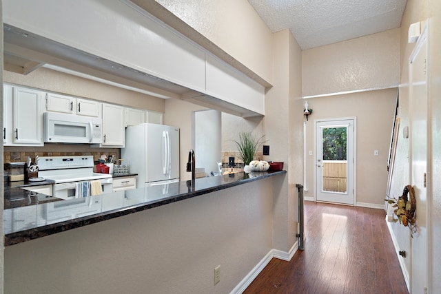 kitchen featuring dark wood-type flooring, kitchen peninsula, dark stone counters, white cabinetry, and white appliances