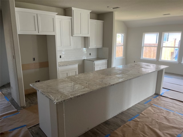 kitchen with light stone countertops, a kitchen island, backsplash, vaulted ceiling, and white cabinets