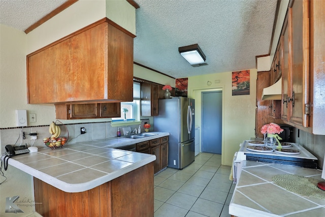 kitchen featuring kitchen peninsula, custom range hood, sink, stainless steel refrigerator, and tile counters