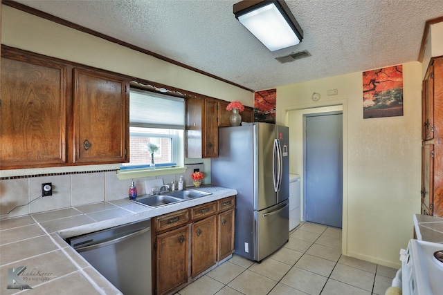 kitchen featuring sink, stainless steel appliances, backsplash, tile countertops, and a textured ceiling