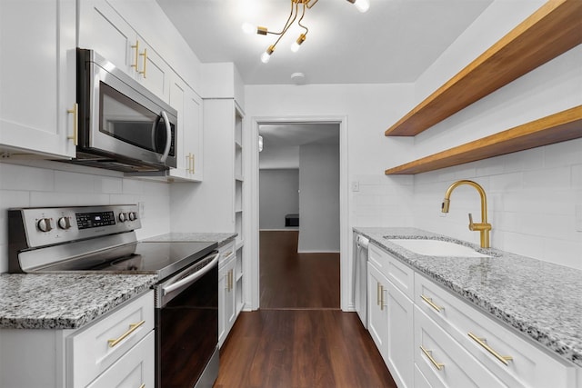 kitchen with appliances with stainless steel finishes, light stone counters, white cabinetry, open shelves, and a sink