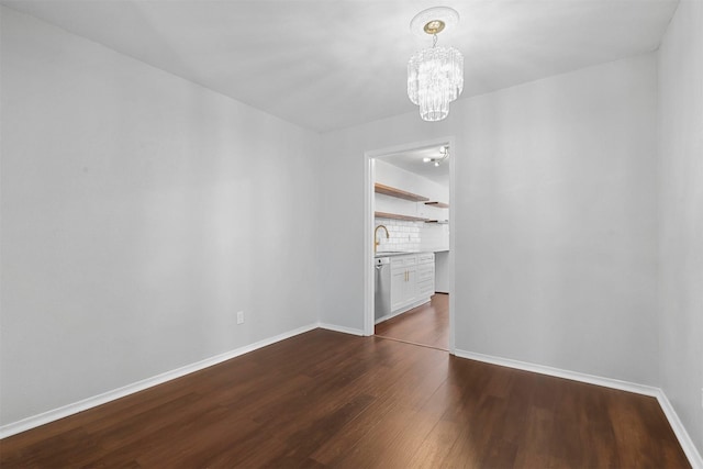 unfurnished dining area with dark wood finished floors, a chandelier, baseboards, and a sink