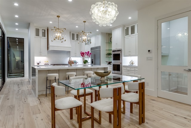 kitchen with white cabinetry, a center island with sink, sink, and hanging light fixtures