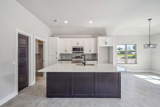 kitchen featuring white cabinets, a center island with sink, light stone counters, appliances with stainless steel finishes, and decorative light fixtures