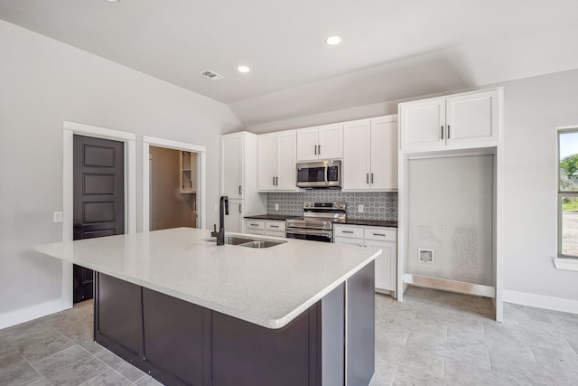 kitchen with lofted ceiling, white cabinets, a center island with sink, sink, and stainless steel appliances