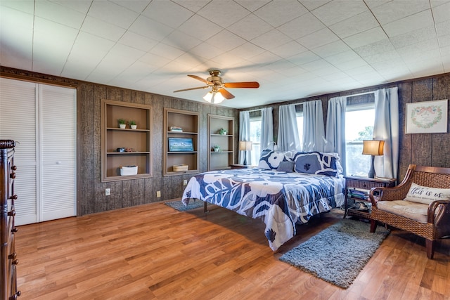 bedroom with wood walls, hardwood / wood-style floors, a closet, and ceiling fan