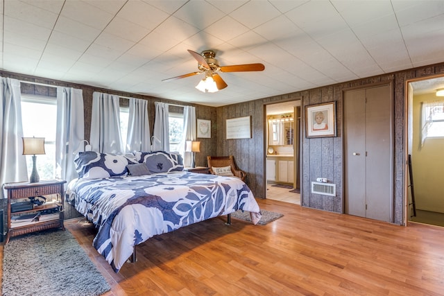 bedroom featuring hardwood / wood-style flooring, wooden walls, connected bathroom, and ceiling fan