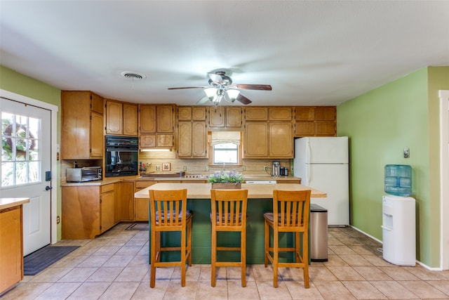 kitchen with oven, ceiling fan, white fridge, decorative backsplash, and a breakfast bar area