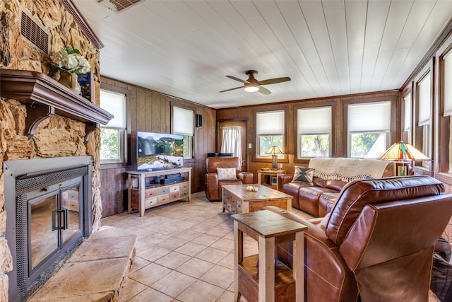 living room with wood walls, wood ceiling, a stone fireplace, light tile patterned floors, and ceiling fan