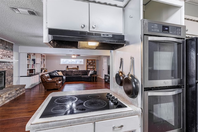 kitchen featuring a fireplace, a textured ceiling, dark hardwood / wood-style flooring, stainless steel double oven, and electric stovetop